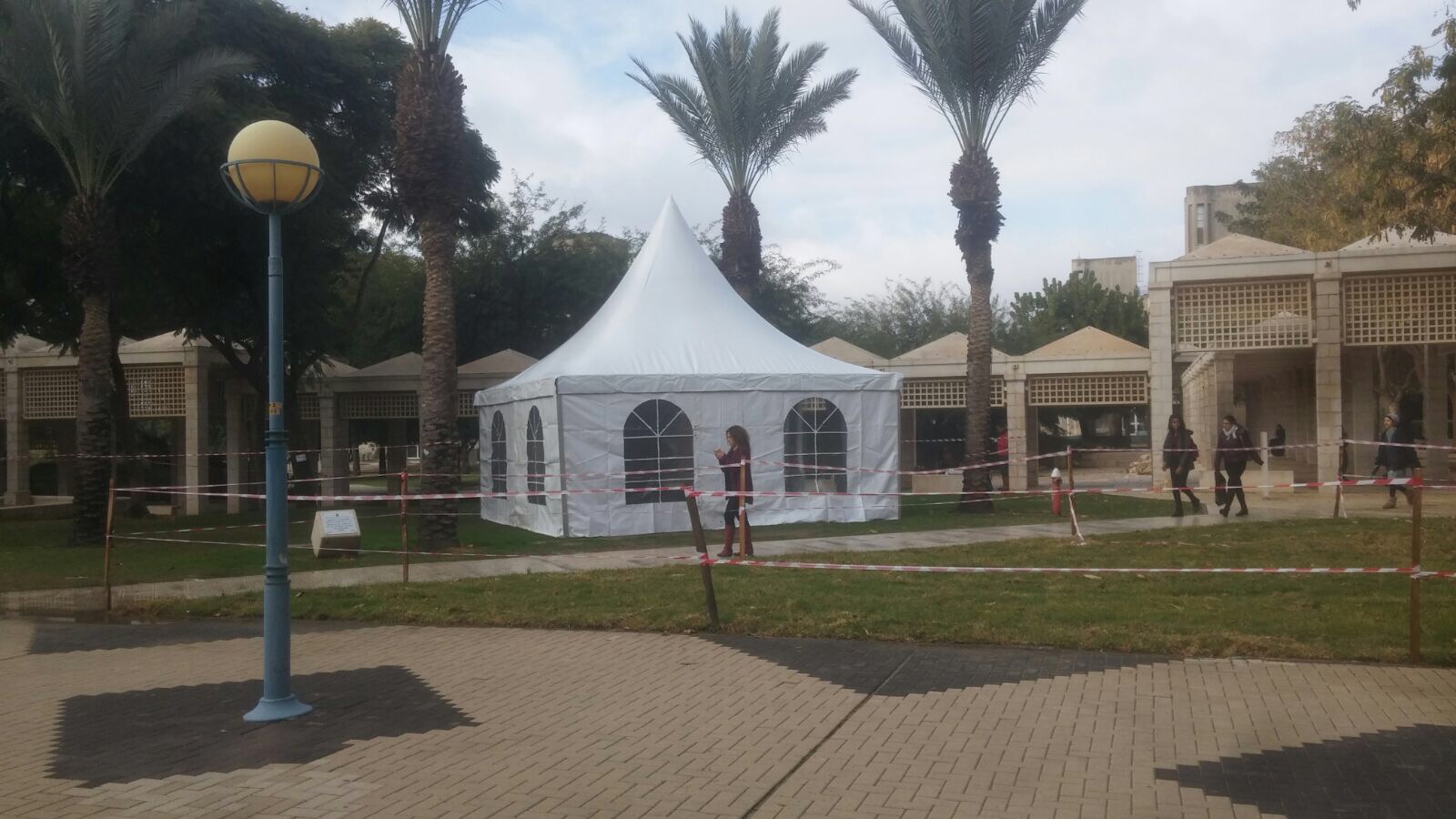 אוהל מסיבות לבן עם גג מחודד מוצב על דשא בפארק, לפני עצים ושיחים.